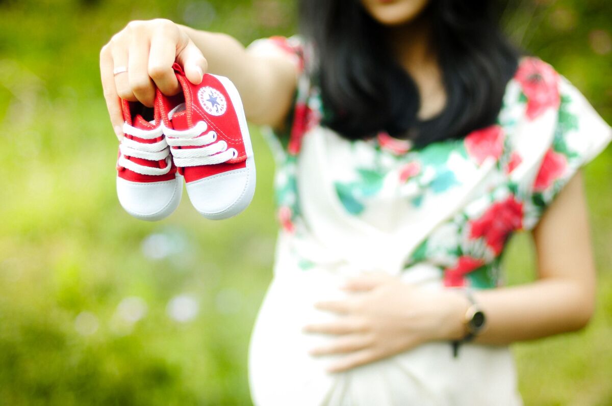 Pregnant woman holding red baby shoes, symbolizing anticipation of a newborn.