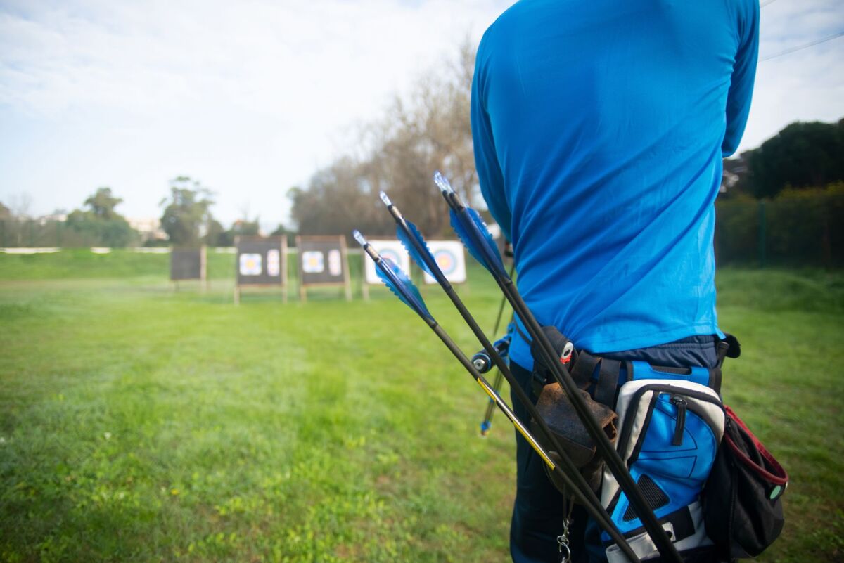 A person in a blue shirt with arrows targets practice in a grassy outdoor setting.