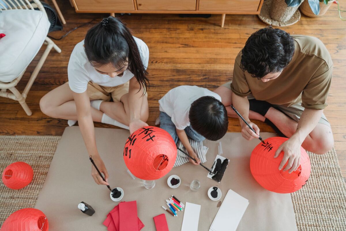 Family enjoying a creative bonding session while painting red lanterns during the day.