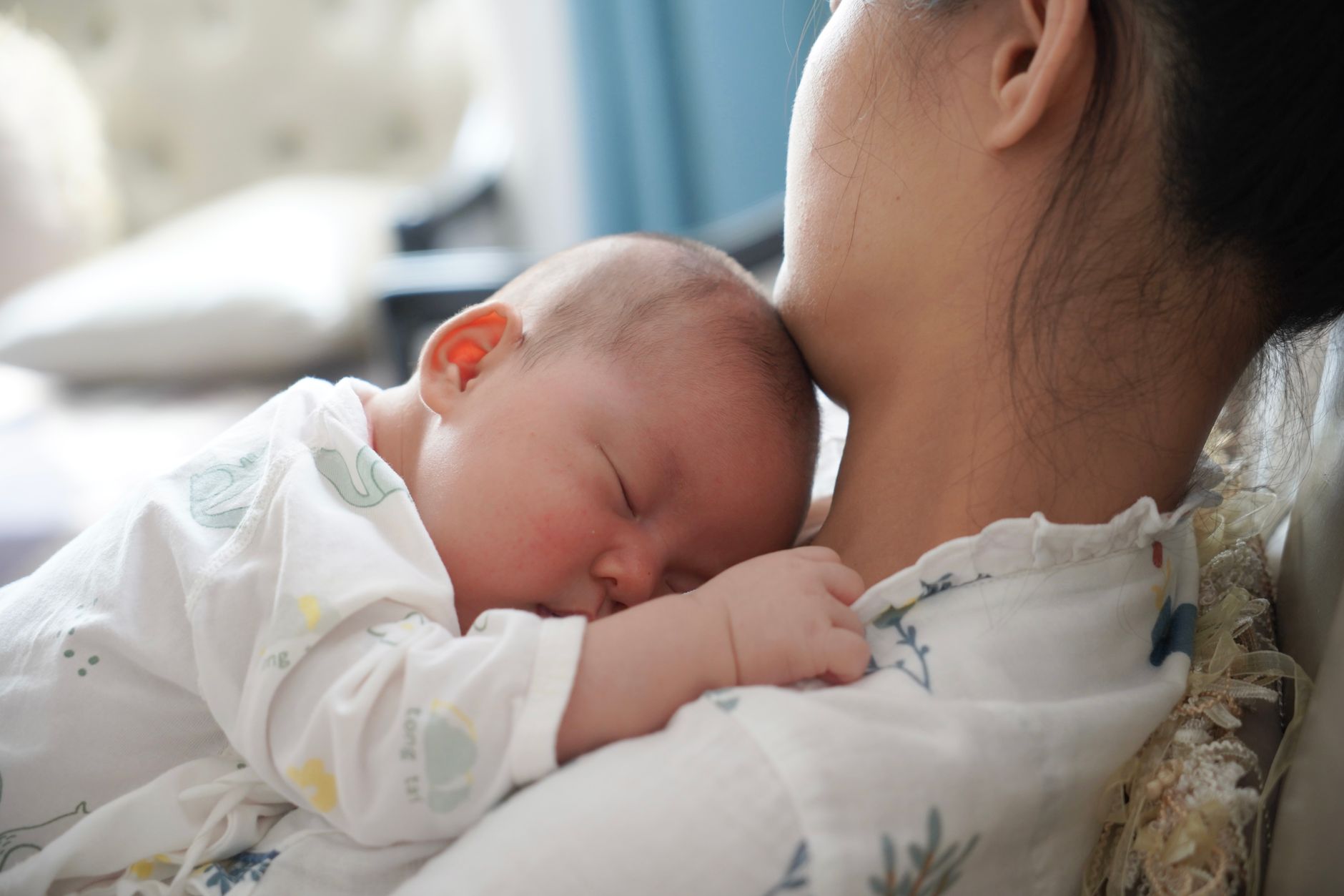 A serene moment of a mother holding her sleeping newborn in a cozy indoor setting.