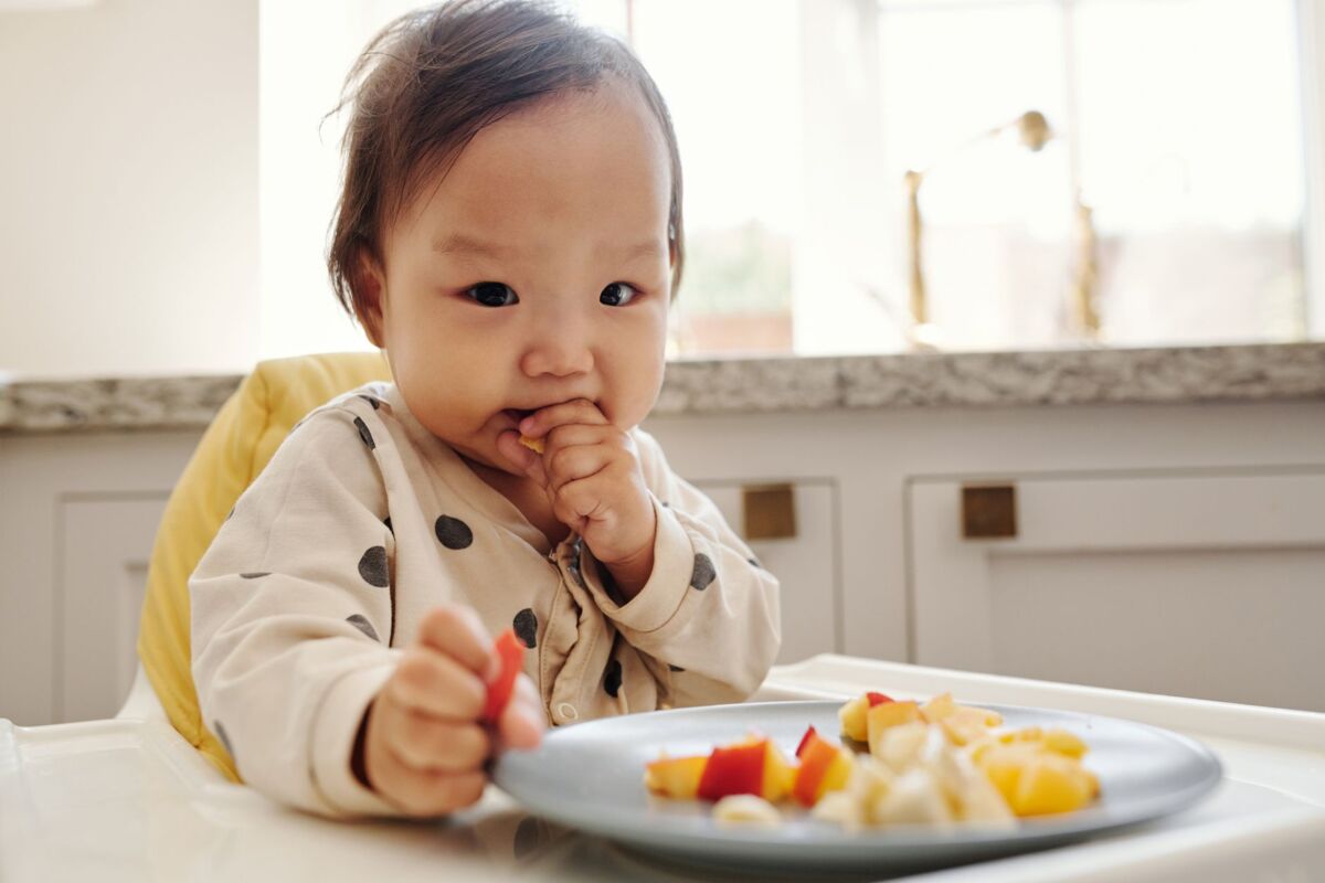 Adorable baby in a polka dot outfit enjoying fresh fruits in a high chair at home.