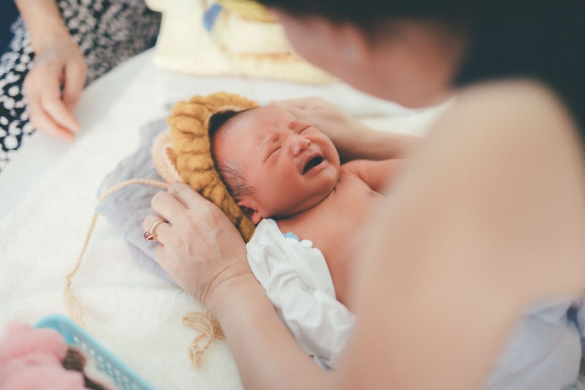 A crying newborn baby lying on a bed while being comforted by a parent, showcasing early life moments.