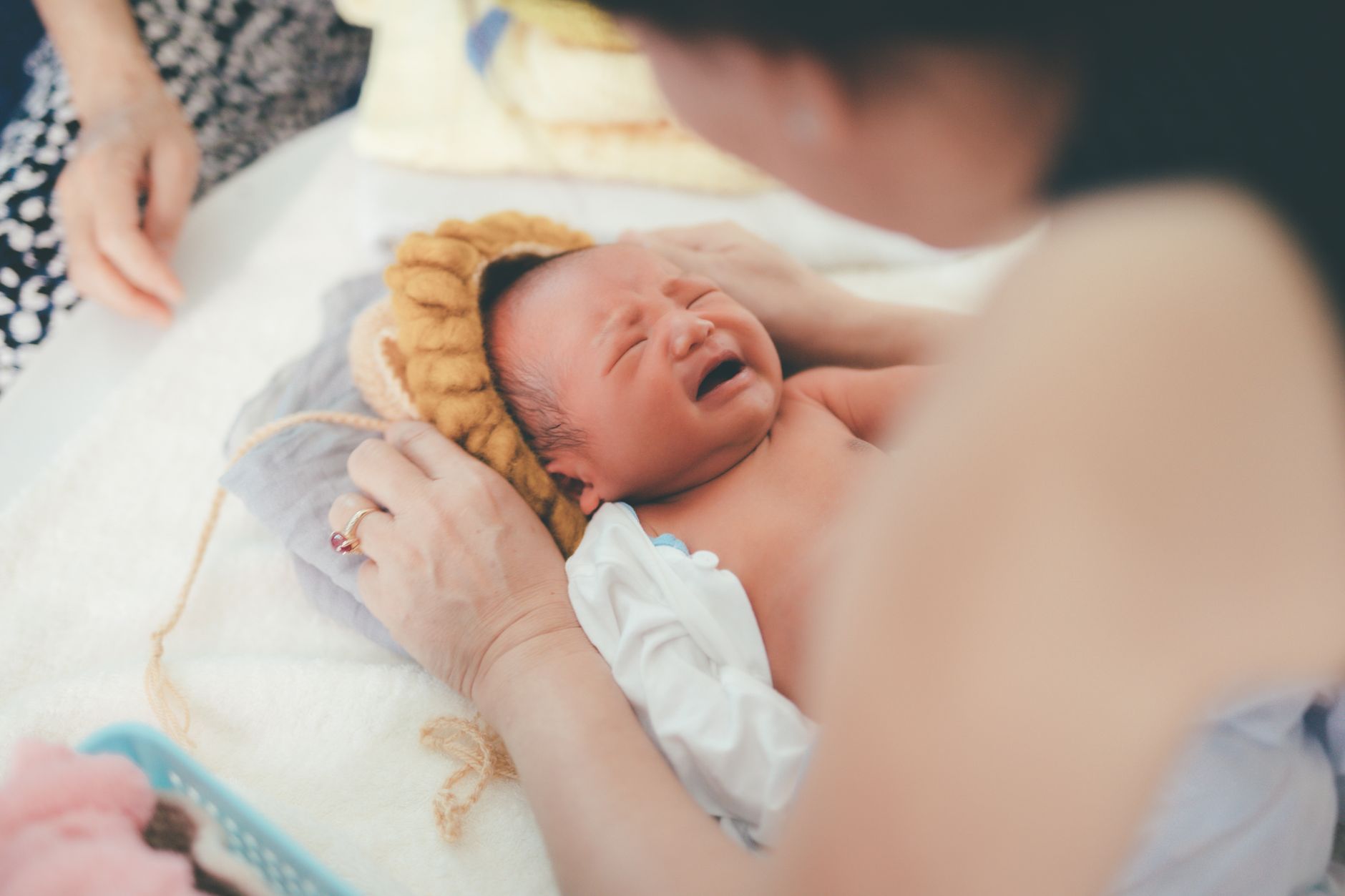 A crying newborn baby lying on a bed while being comforted by a parent, showcasing early life moments.