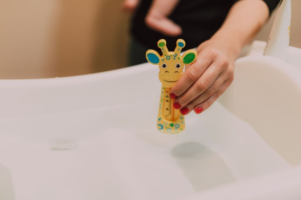 A hand holding a giraffe-shaped thermometer in a baby bath for temperature check.
