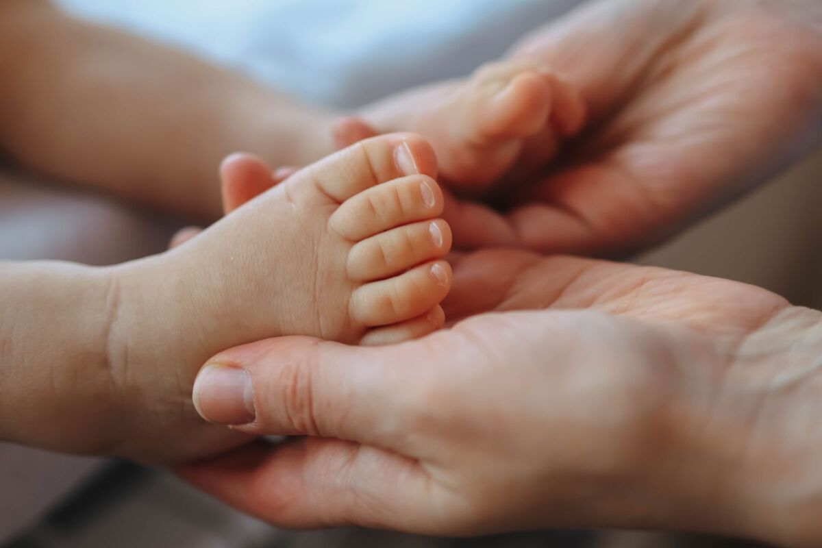 Close-up of a parent's hands gently cradling a newborn's foot, symbolizing care and tenderness.