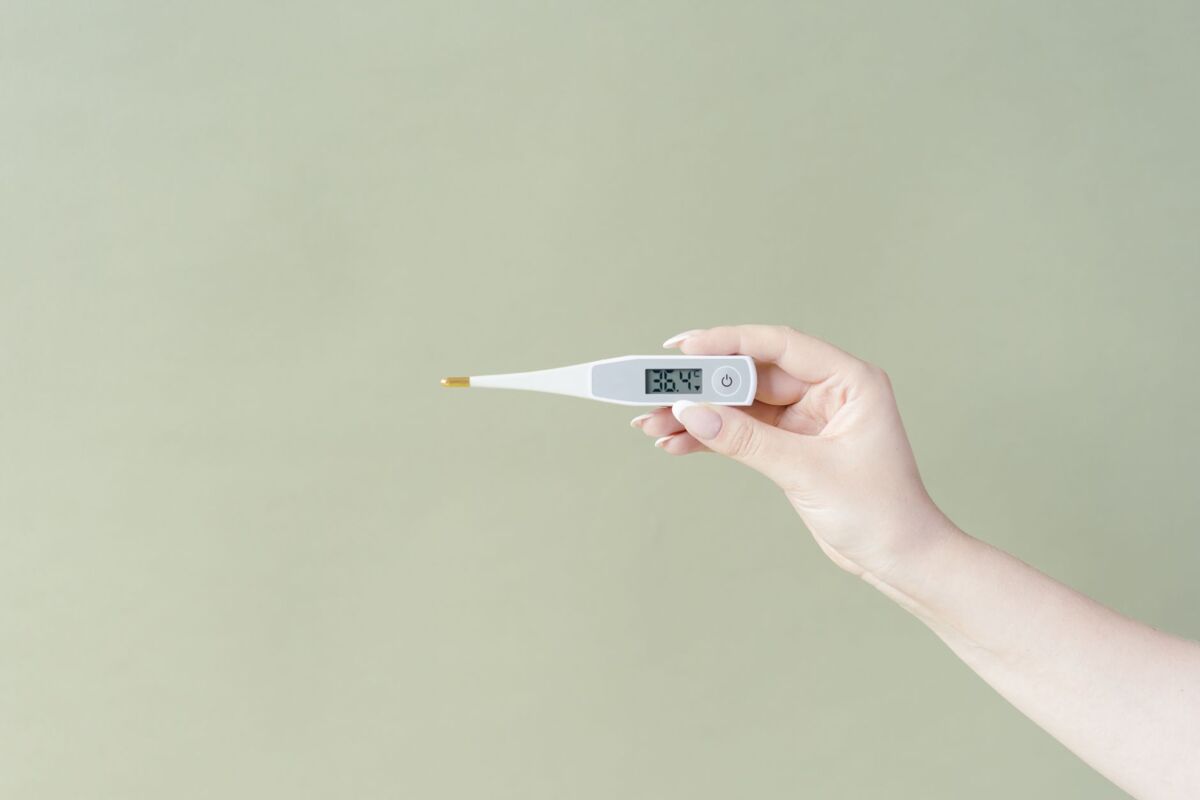 Hand holding a digital thermometer displaying 36.4C on a light green background, minimalistic style.
