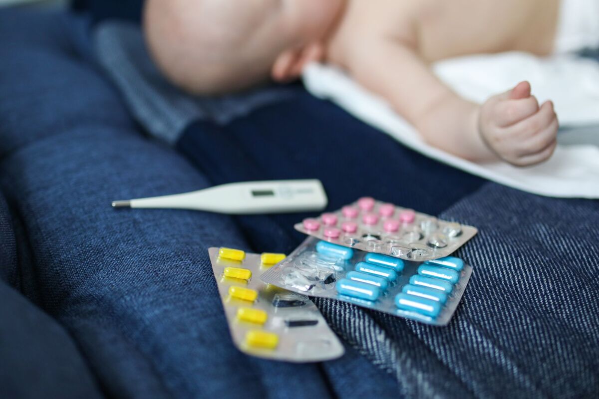 A baby lying next to various medications and a thermometer, suggesting health issues.