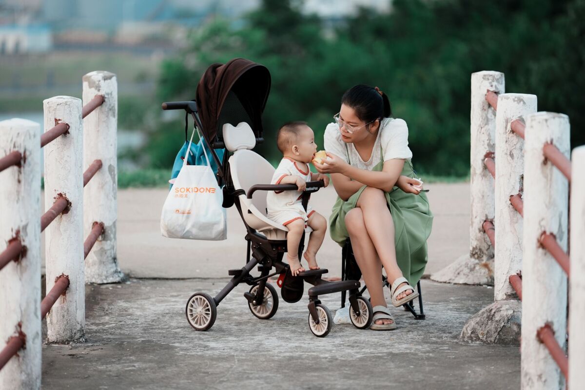 A mother lovingly feeds her baby while sitting outdoors with a stroller.