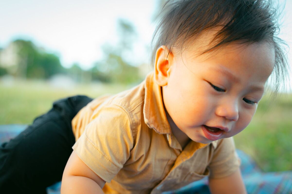 Adorable Asian child with black hair crawling on a blanket outdoors, enjoying a sunny day.