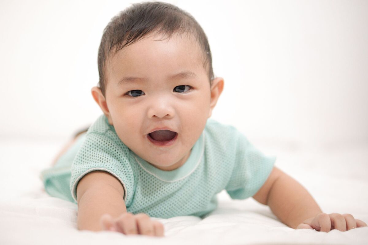 A cute Asian baby boy smiling while lying on a white background.