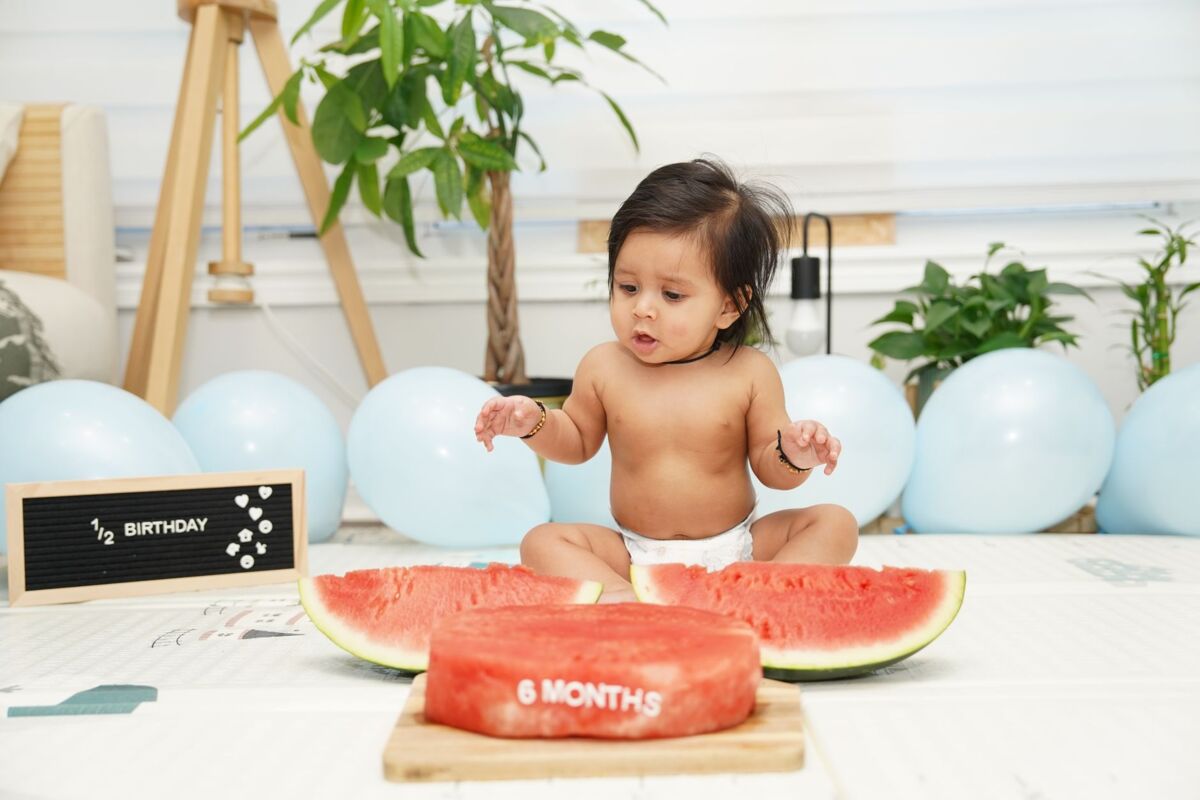 Cute baby celebrating six-month birthday with watermelon and festive decor.