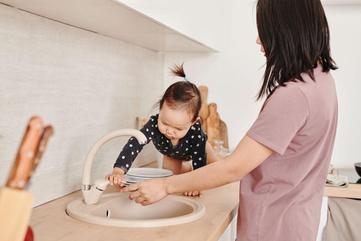 Cute toddler playing at the kitchen sink with mother supervising.