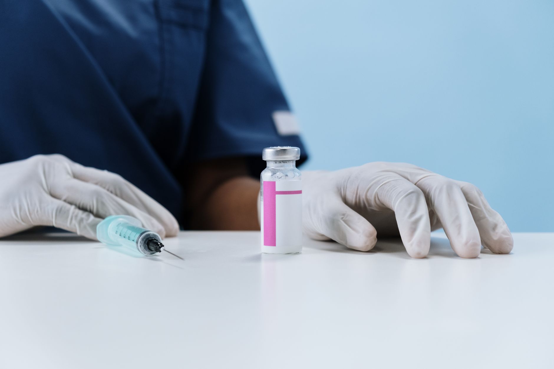 Close-up of healthcare worker's gloved hands with syringe and vaccine vial on a table.
