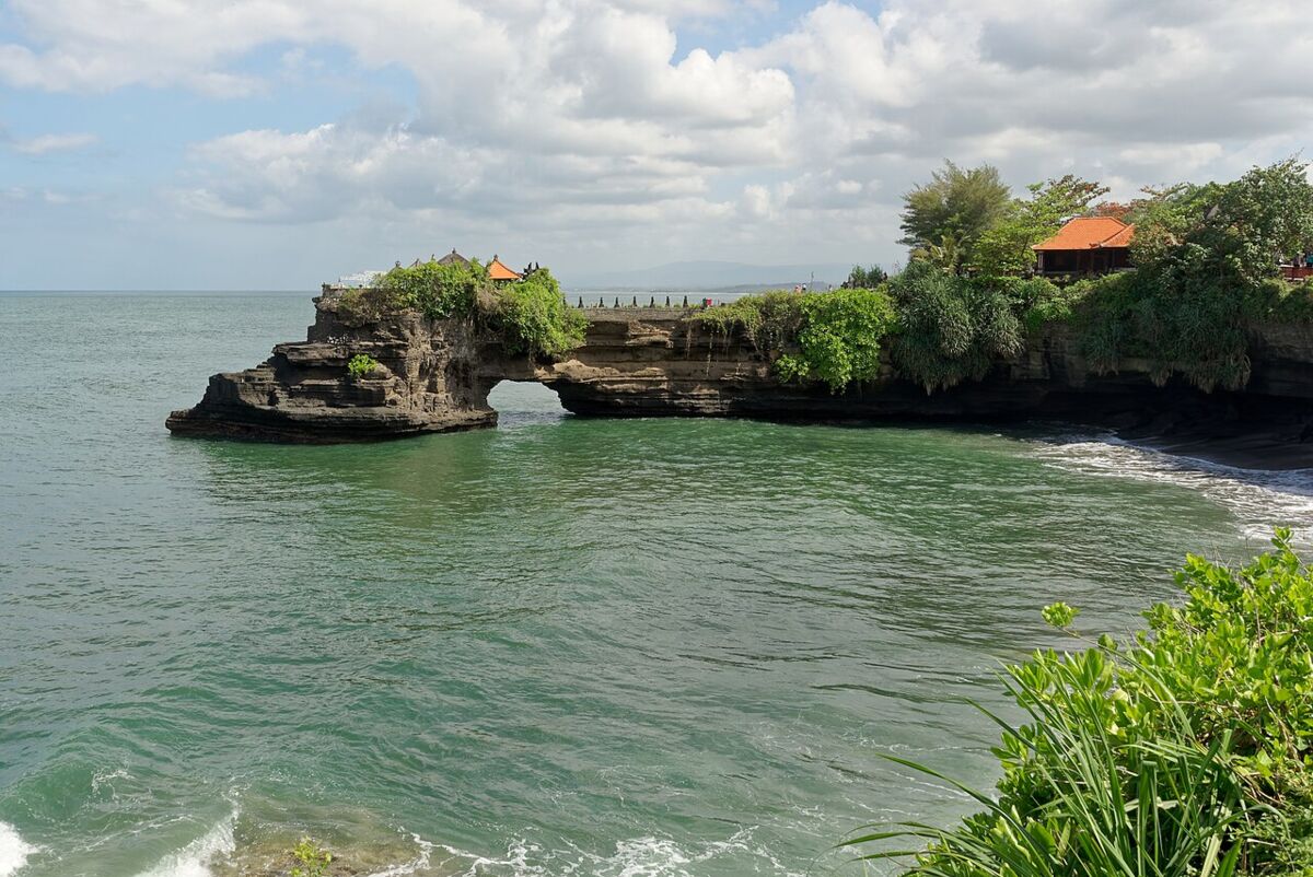 Batu Bolong sea temple on a rocky cliff arch above turquoise water near Tanah Lot, Bali