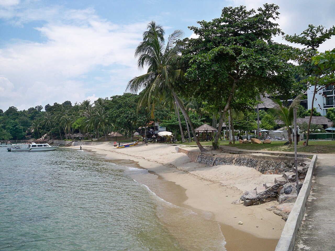 Sandy beach lined with palm trees and a moored boat at Turi Beach Resort, Batam