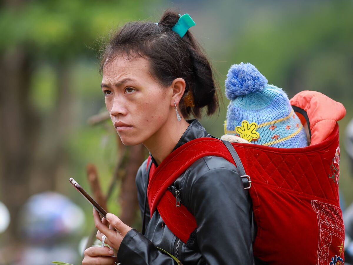 Hmong woman carrying her baby in a traditional carrier, outdoors in Lao Cai, Vietnam.