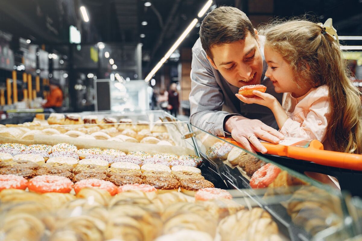 A father and daughter share a bonding moment choosing donuts at an indoor supermarket.