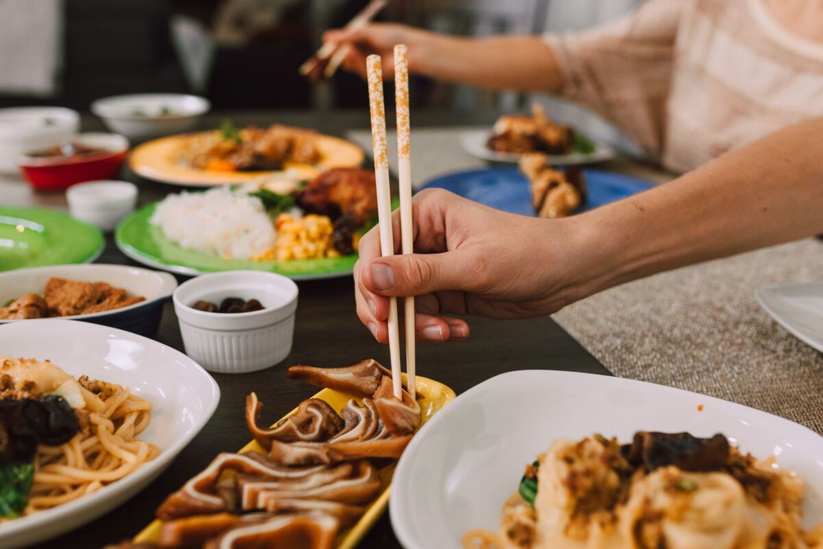 Close-up of hands using chopsticks to enjoy a variety of Asian dishes at a dining table.
