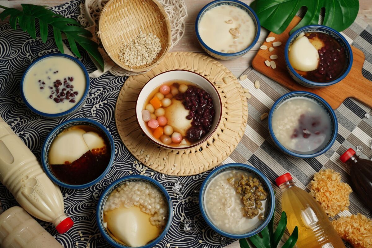 Top view of assorted Asian desserts featuring tofu pudding, rice, and syrup in ceramic bowls with decorative elements.