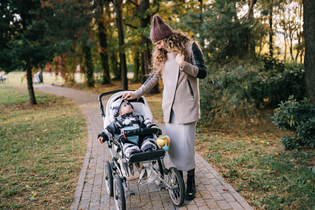 A mother enjoys a walk with her baby in a stroller through a scenic park during autumn.