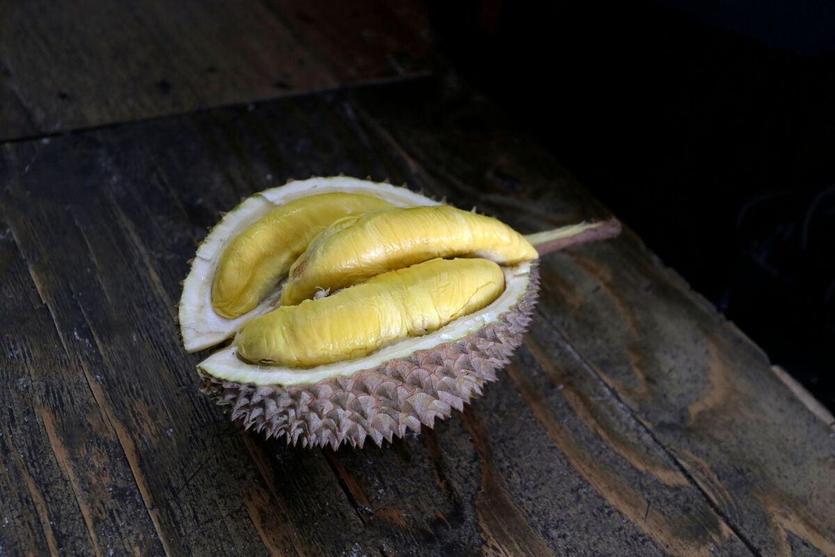 Close-up of a durian fruit split open, revealing yellow flesh on a wooden surface.