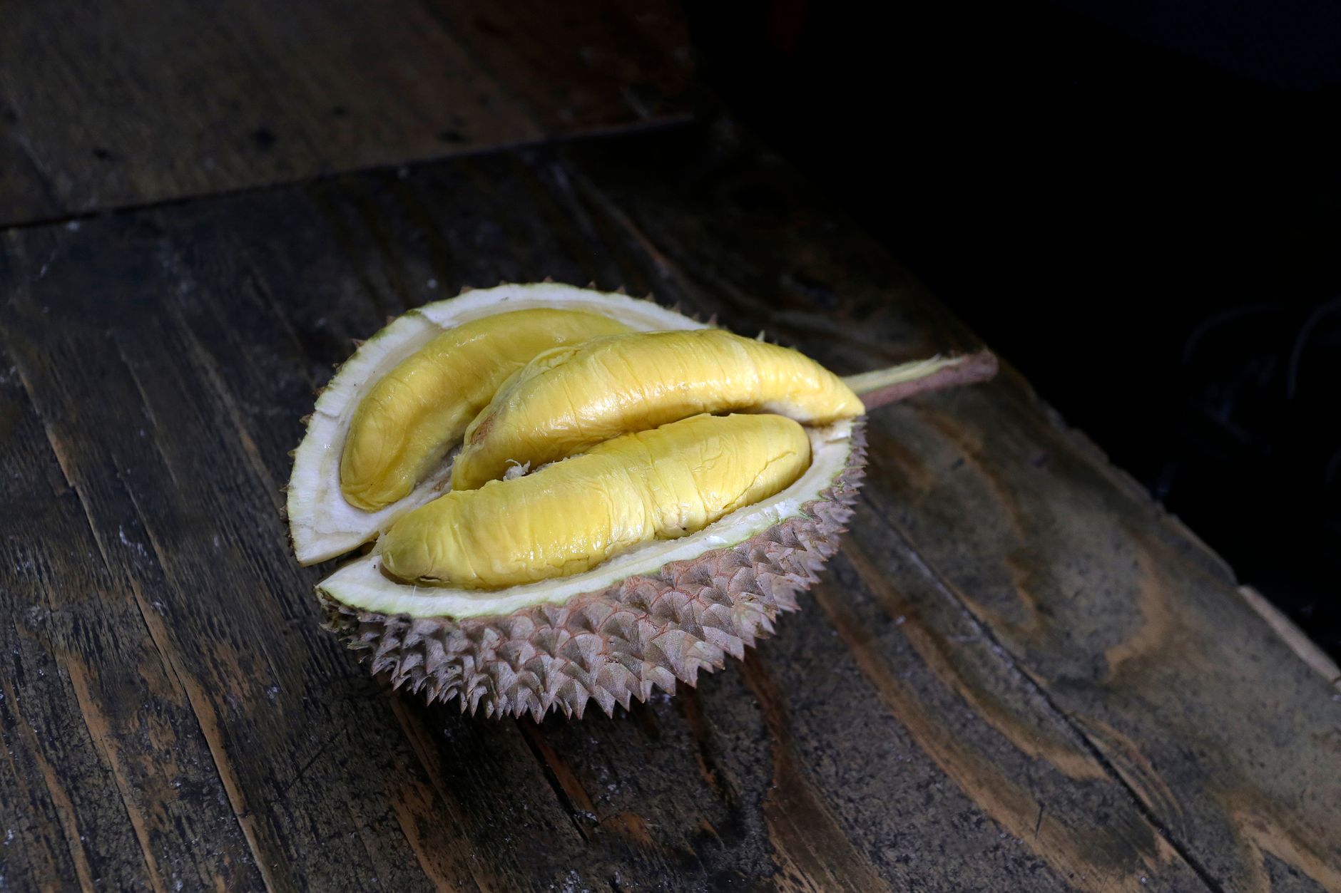 Close-up of a durian fruit split open, revealing yellow flesh on a wooden surface.