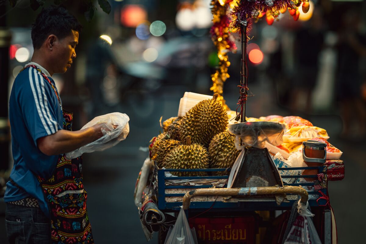 A street vendor prepares durian for sale in Bangkok's vibrant night market.