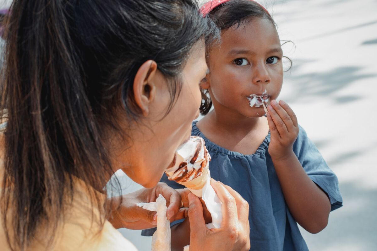 Crop anonymous ethnic mother eating and sharing delicious sweet ice cream with adorable little daughter