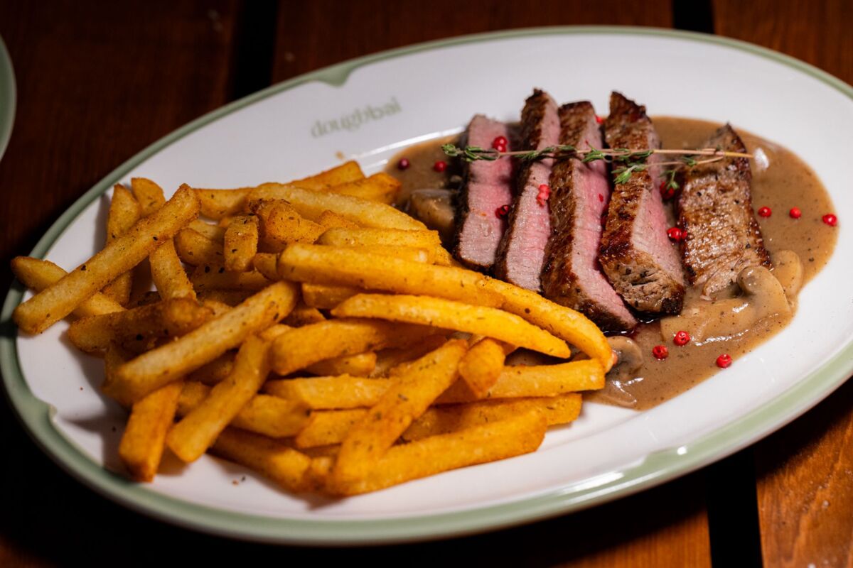 Sliced steak with fries and sauce on a ceramic plate, gourmet meal.