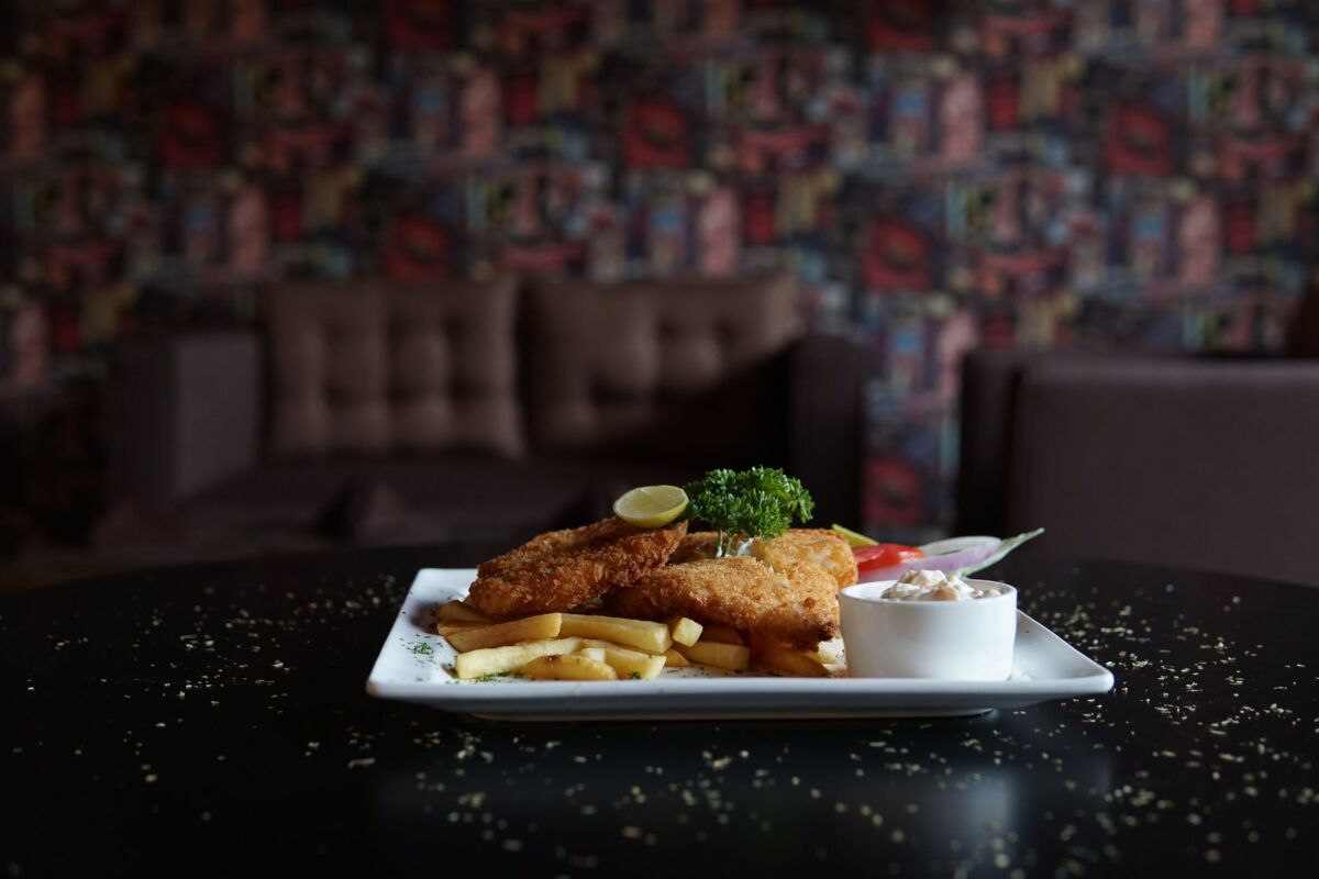 Crispy fish and chips served with garnish and dip in a cozy indoor setting.
