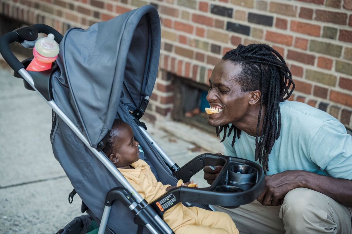 A joyful father engages playfully with his baby in a stroller outdoors.