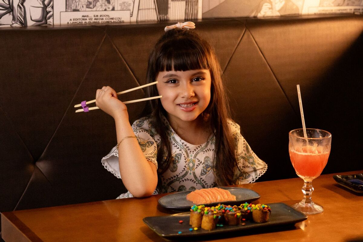 Charming young girl in a restaurant using chopsticks, enjoying sushi and a colorful dessert.
