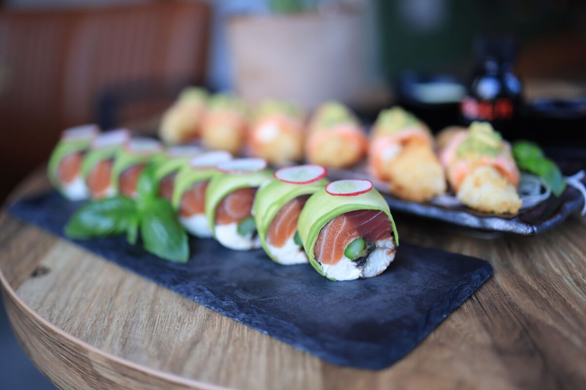 Close-up of sushi rolls with avocado and salmon, garnished with fresh basil on a slate platter.