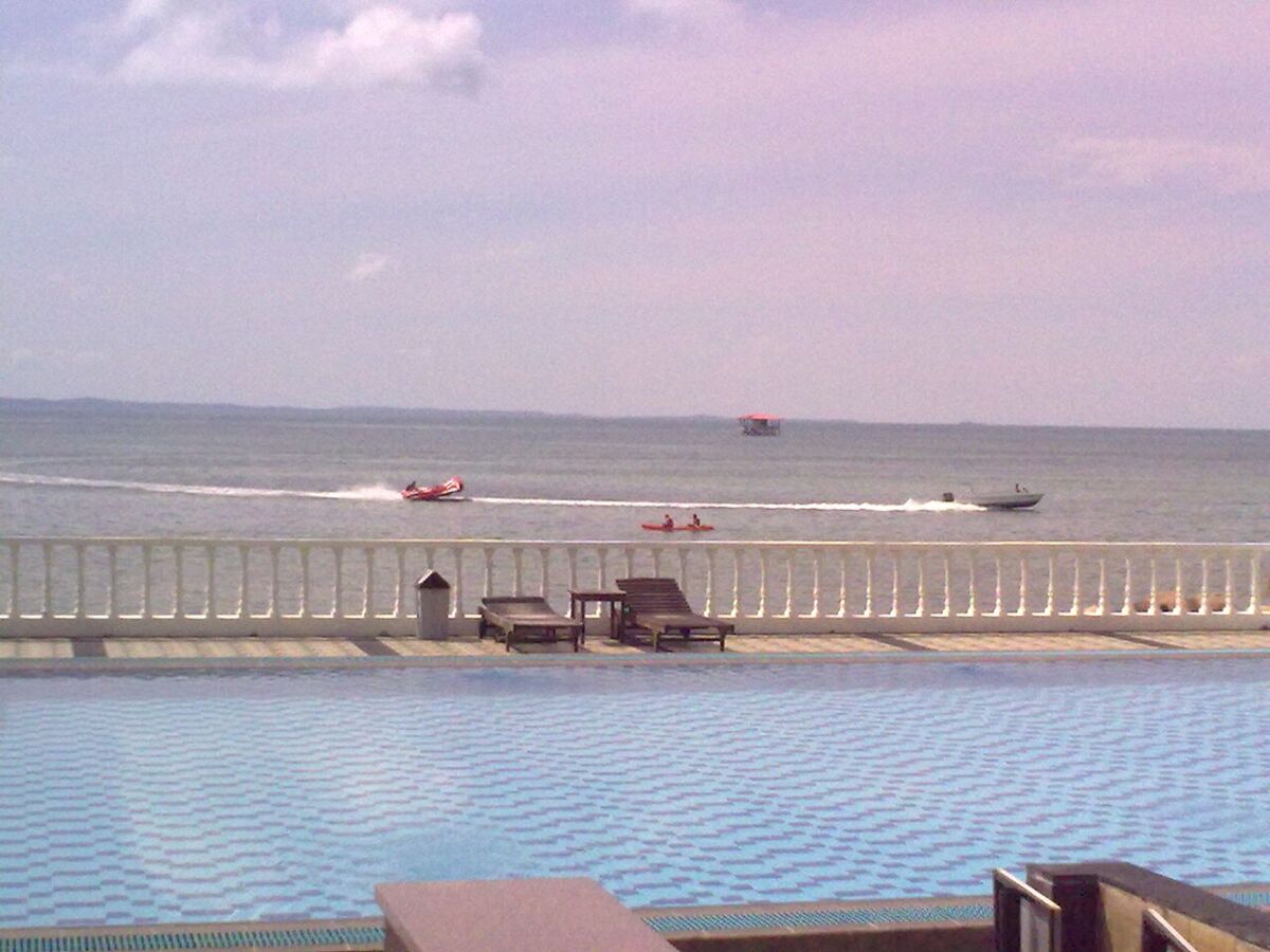 Seaside infinity pool with sun loungers overlooking the sea and watersports at a Bintan resort