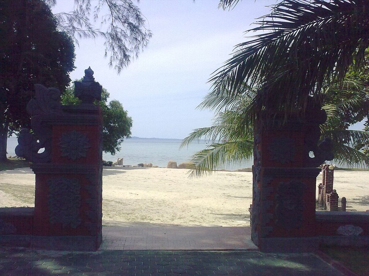 Carved Balinese-style stone gateway opening onto a sandy beach and calm sea at Bintan