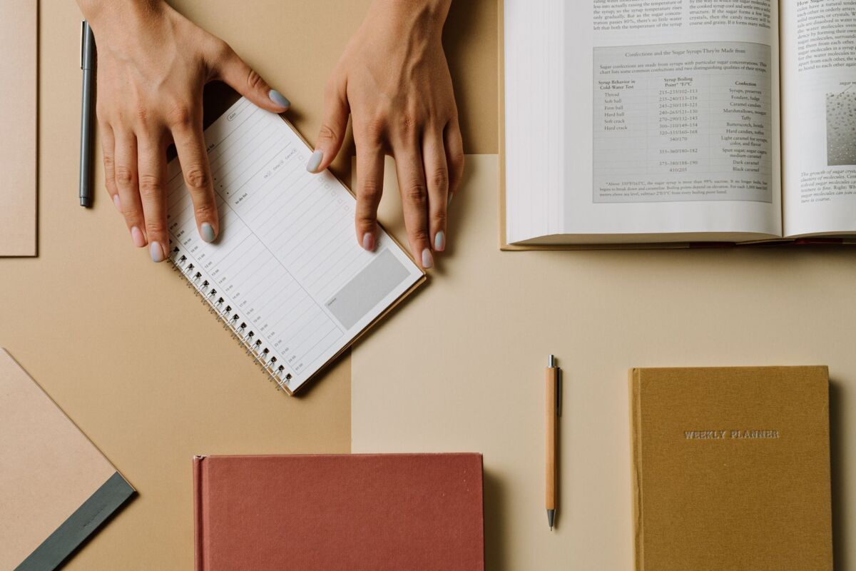 Top view of hands arranging books and planners on a desk.