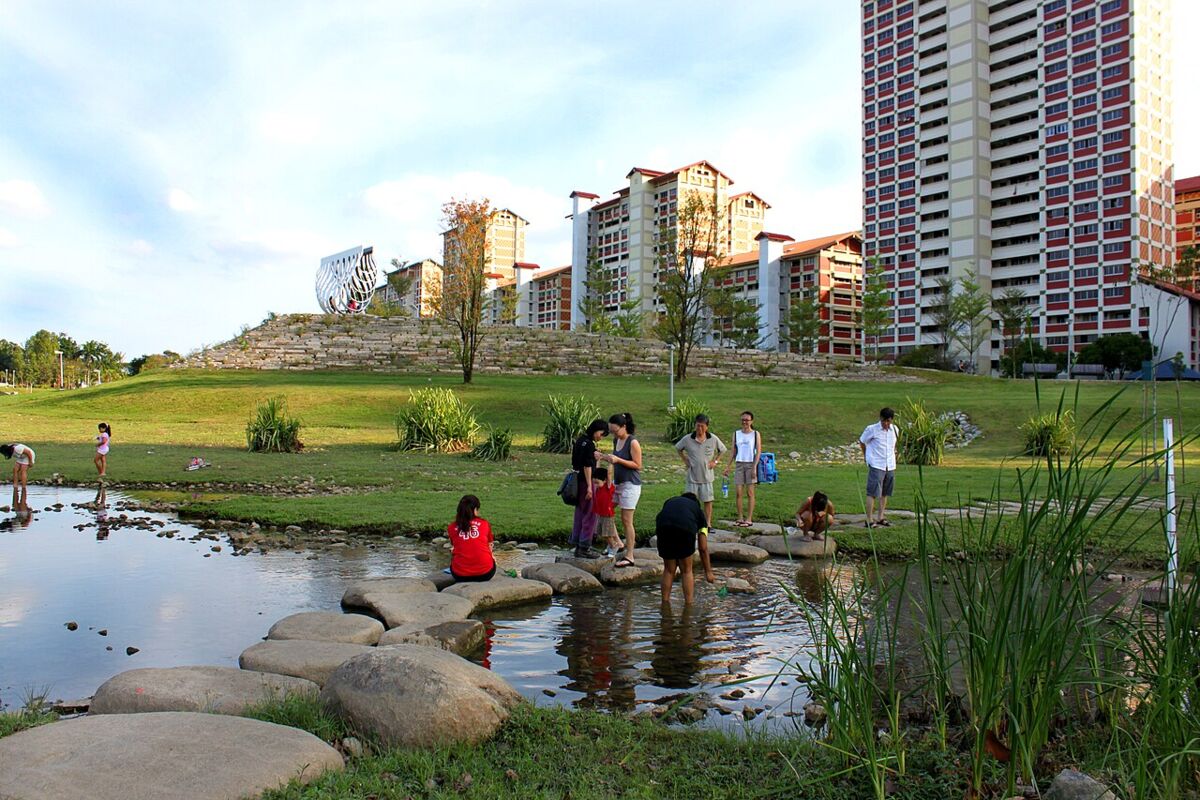 Children and families exploring the stepping stones and shallow river edge at Bishan-Ang Mo Kio Park with HDB flats behind