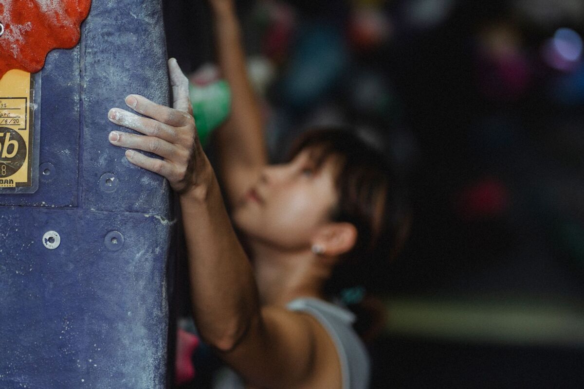 Side view focused young Asian female in sportswear with chalk on hands climbing wall in modern sports center and looking up