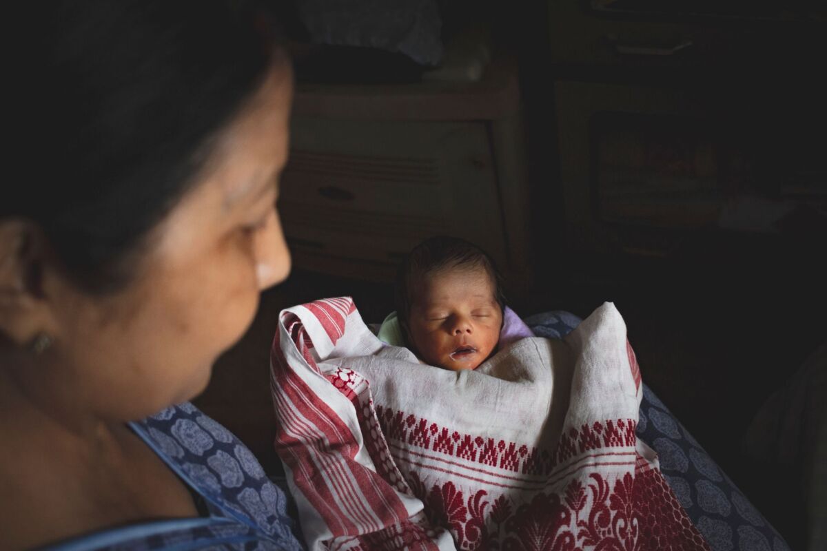 A peaceful scene with a mother and sleeping newborn wrapped in traditional fabric.