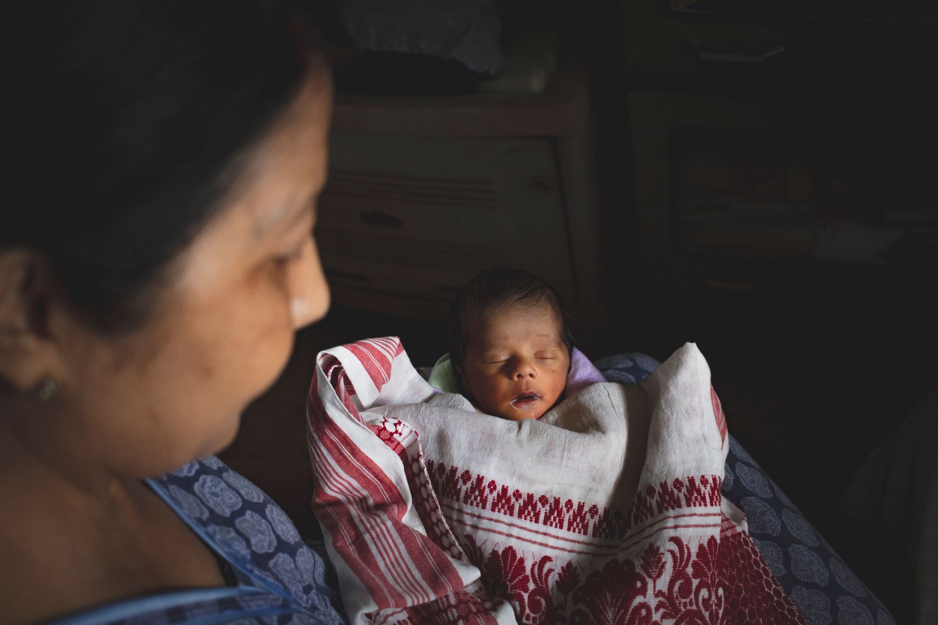 A peaceful scene with a mother and sleeping newborn wrapped in traditional fabric.