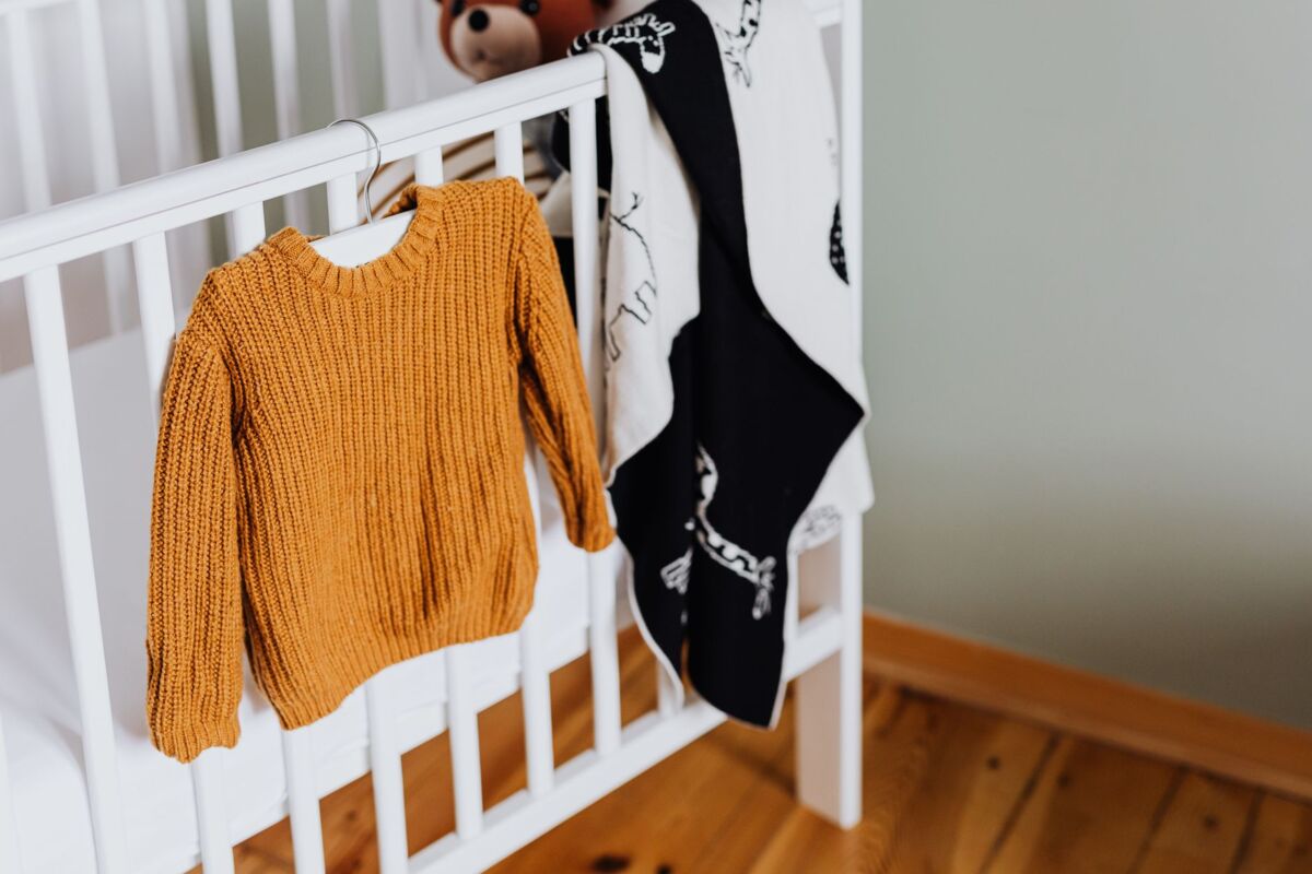 Warm mustard knitted baby sweater hanging on a white crib in an inviting nursery setting.