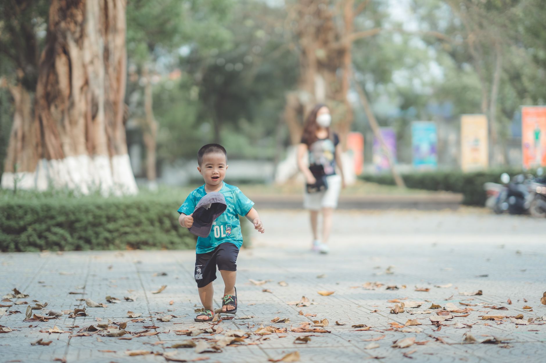 Asian boy in a blue shirt joyfully running in a sunlit park during daytime.