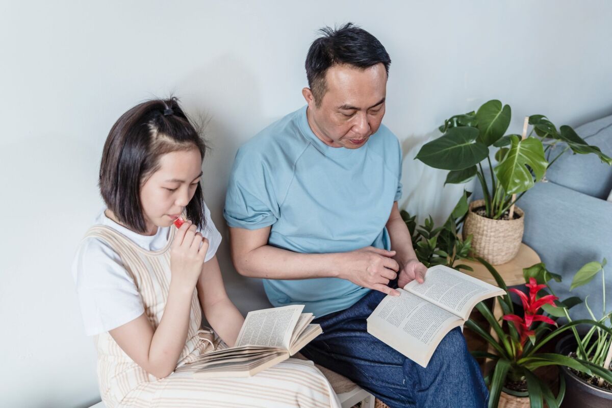 Father and daughter enjoying a quiet reading session indoors surrounded by plants.