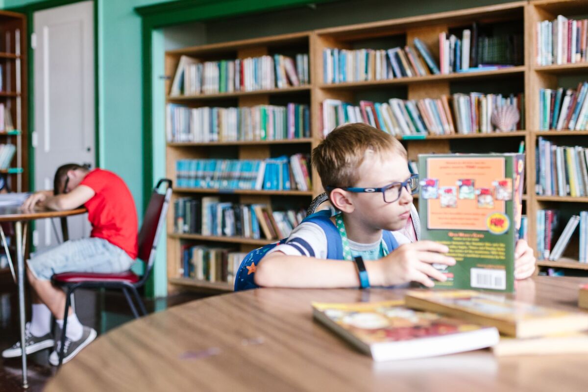 Young boy focused on reading a book in a vibrant school library environment.