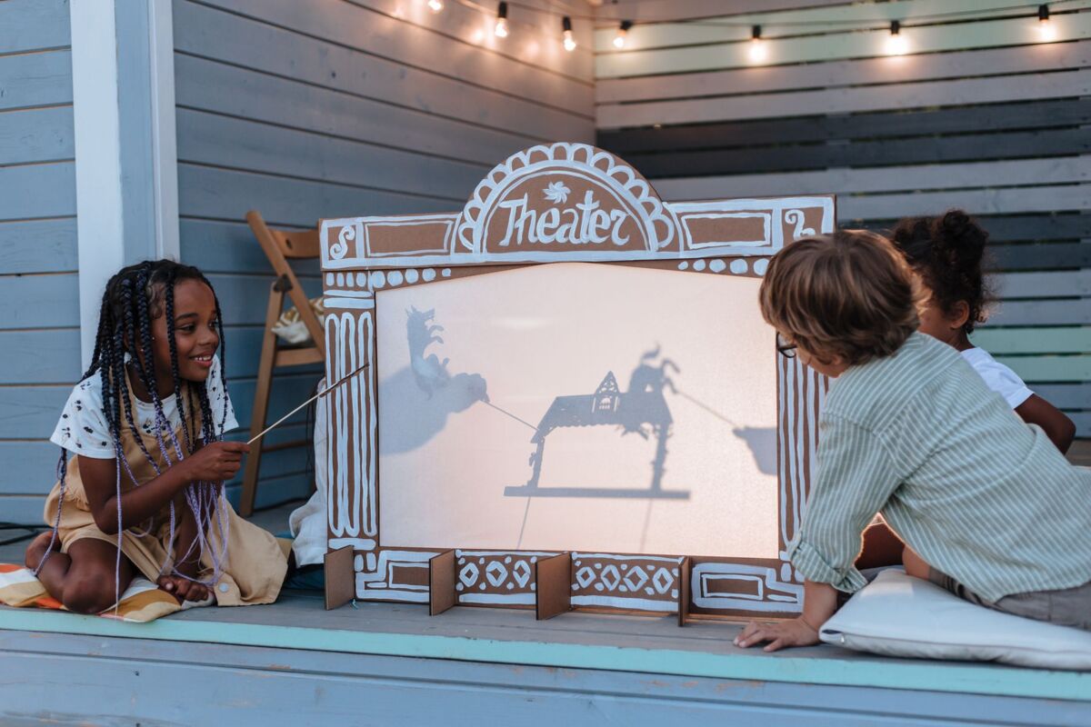 Children playing with a DIY shadow puppet theatre on a deck. Creative play under strings of lights.