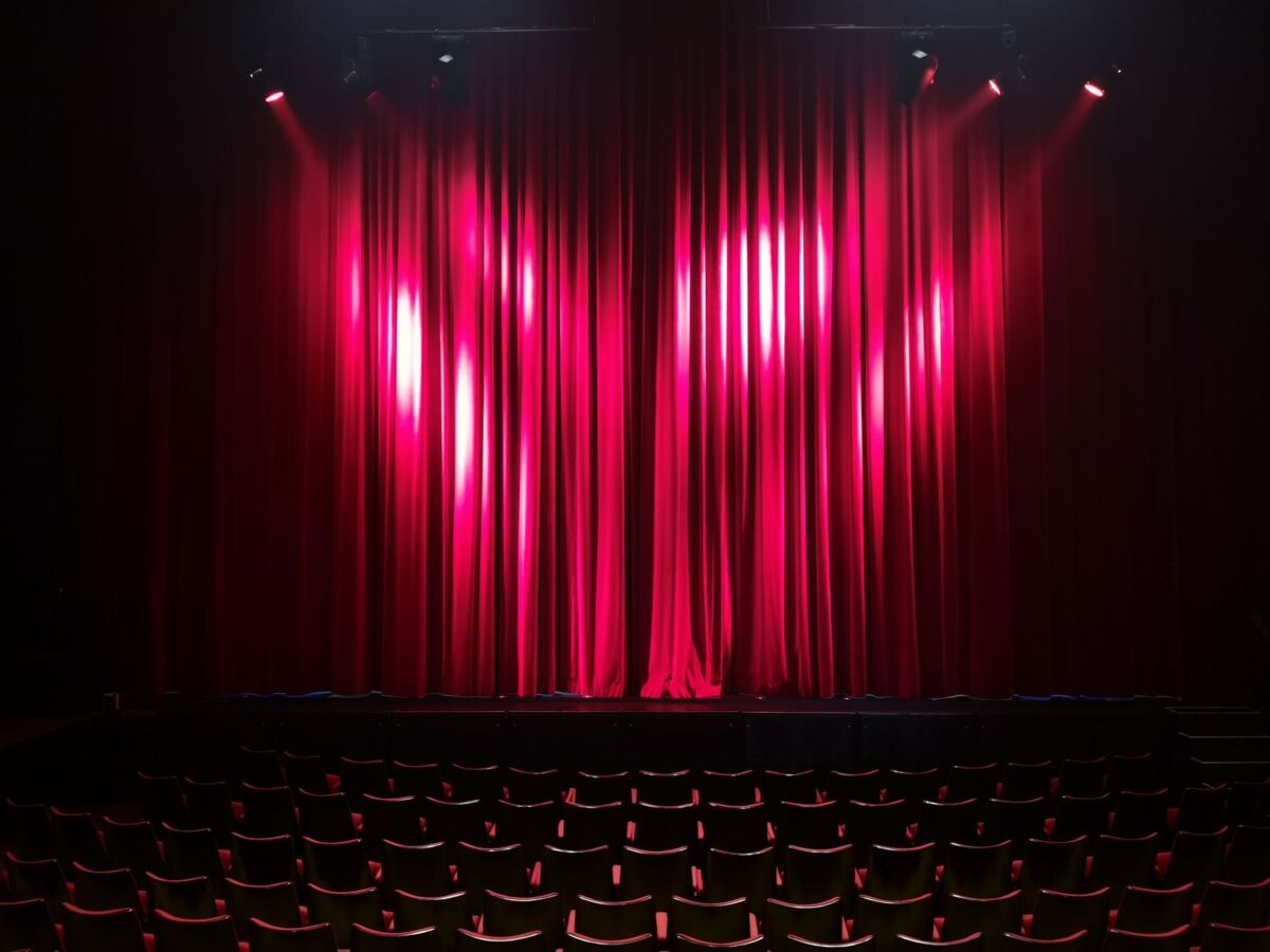 Empty theater stage with red curtains and seating, ready for a performance.