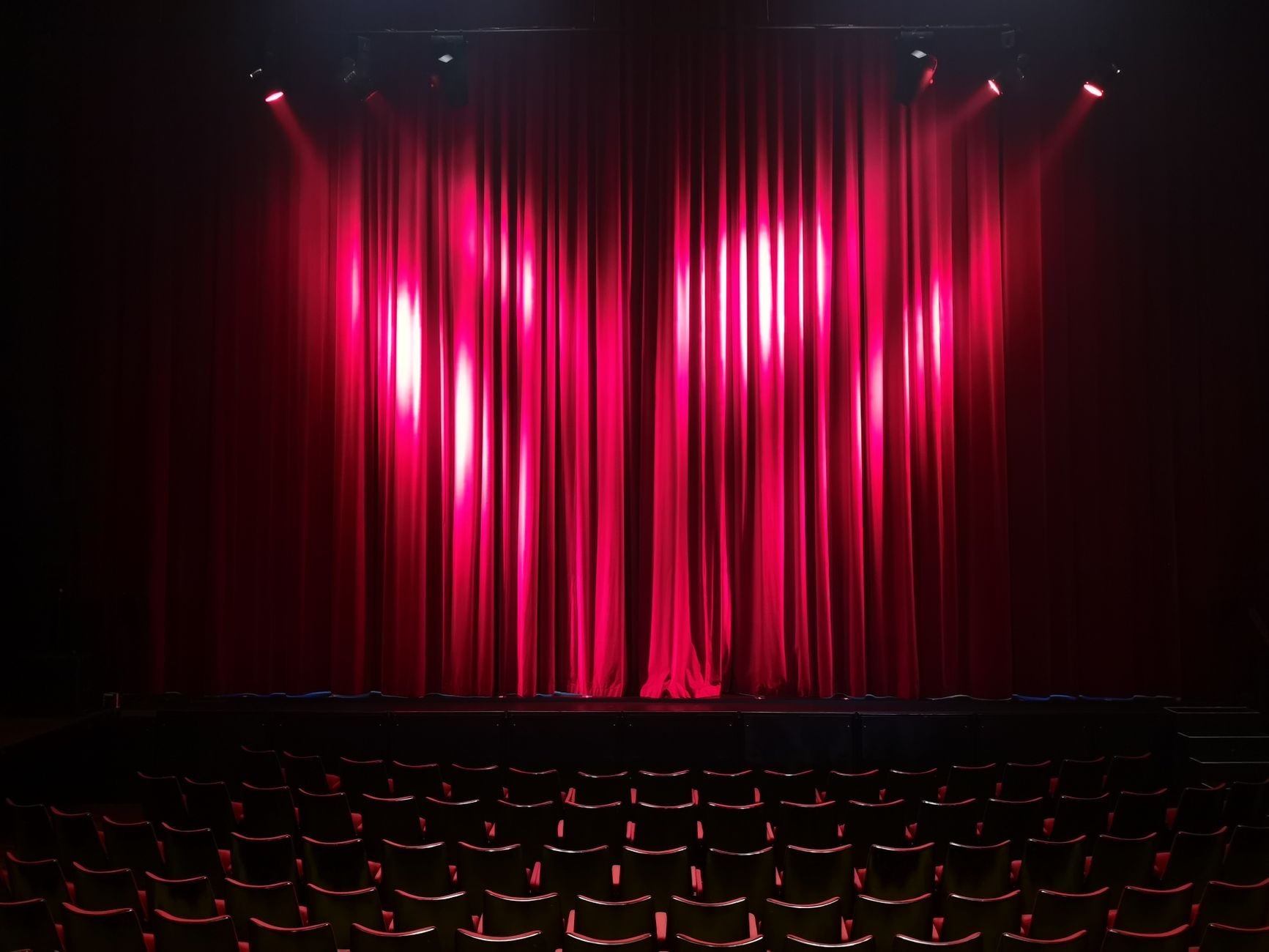 Empty theater stage with red curtains and seating, ready for a performance.