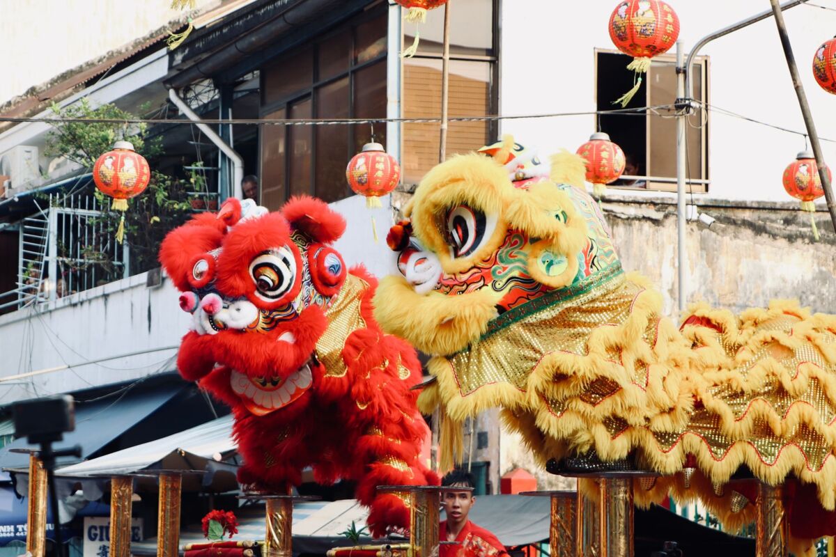 Colorful lion dance performance with red and yellow costumes at a cultural festival, featuring traditional lanterns.