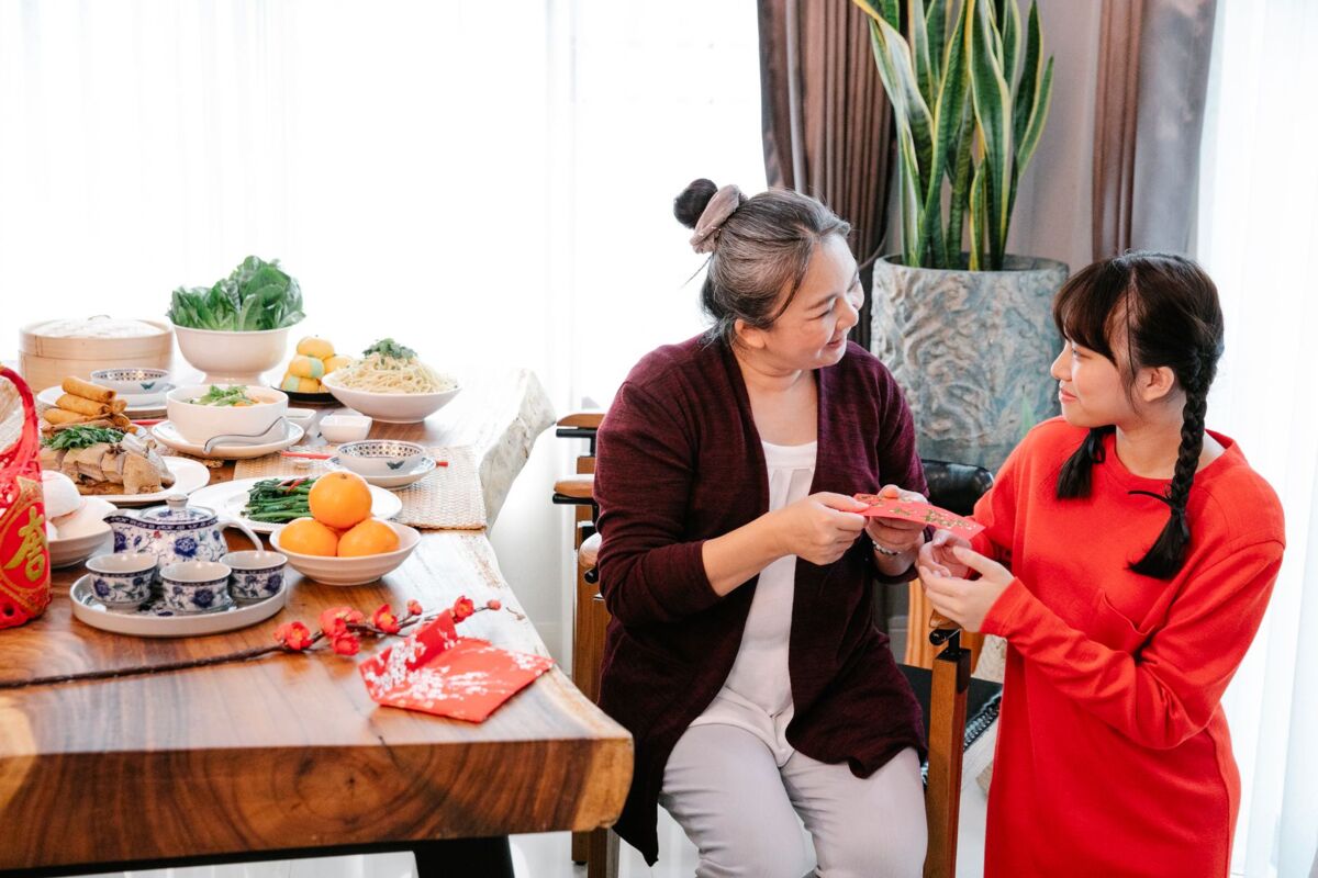 Content ethnic grandmother with envelope speaking with female teen while looking at each other during festive event in house room