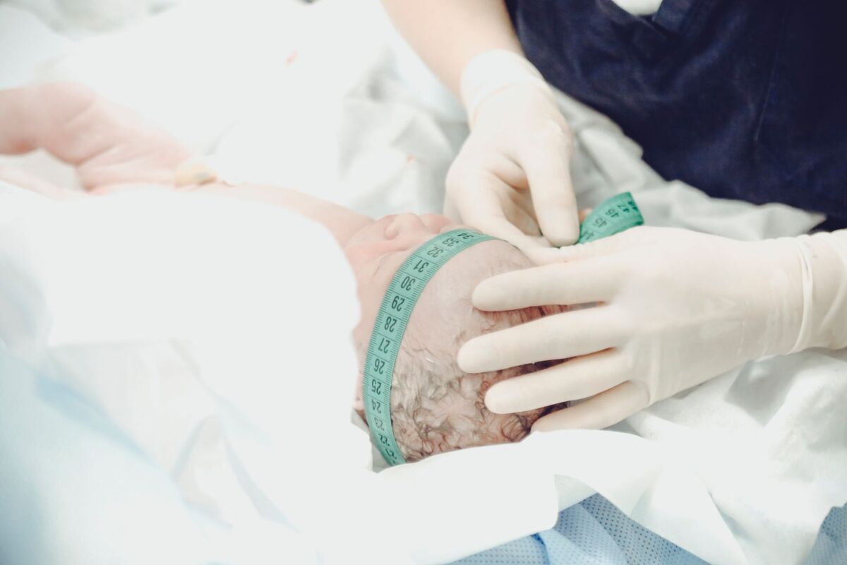 A healthcare professional measures a newborn baby's head circumference in a hospital setting.